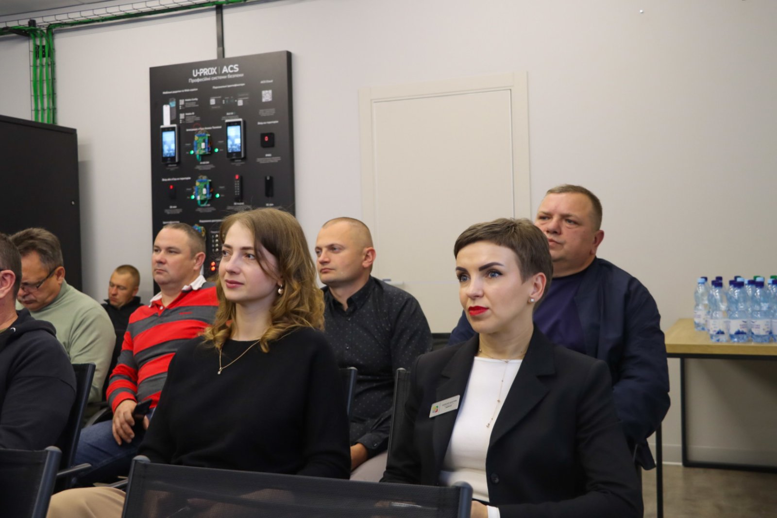 Група людей сидить у приміщенні, спереду - дві жінки.